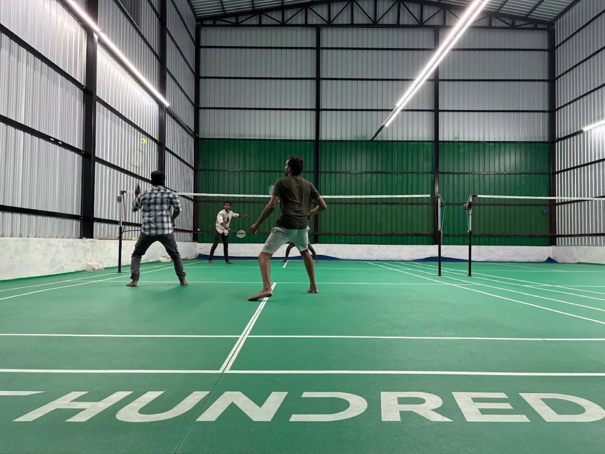 Badminton court with green flooring at Idigarai, Coimbatore, with players mid-rally