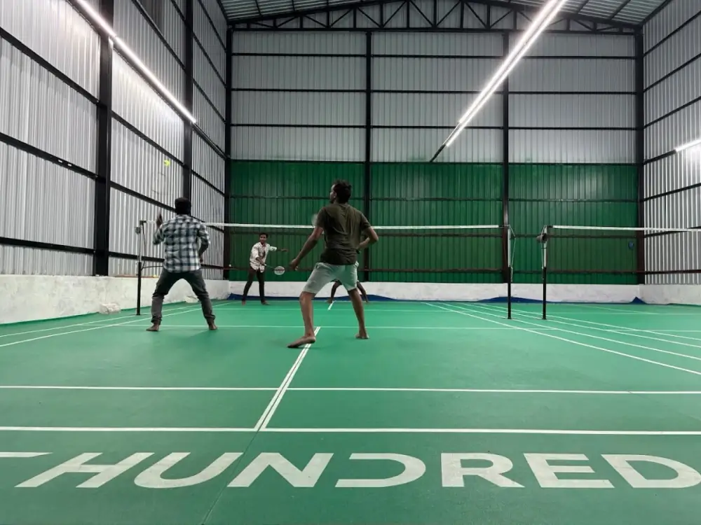 Badminton court with green flooring at Idigarai, Coimbatore, with players mid-rally